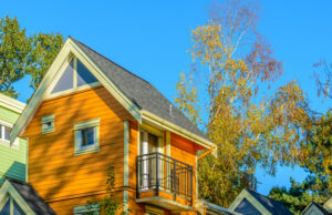 Exterior view of a two-story wooden home with a balcony against clear blue sky and trees.